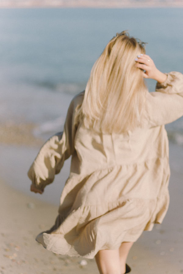 Mujer con vestido beige caminando por la playa